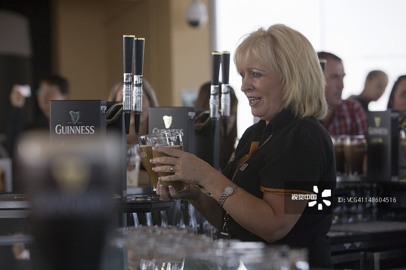 友好的酒保在吉尼斯啤酒厂的重力酒吧里倒一杯品脱的吉尼斯啤酒。图片素材