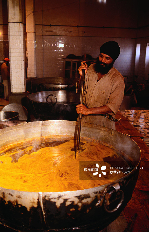 男子在加尔各答的锡克教寺庙厨房里搅拌一大锅藏红花扁豆图片素材