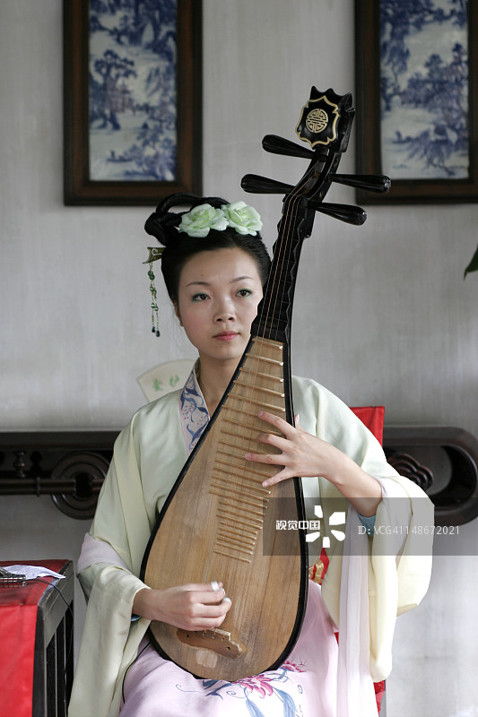 年轻女音乐家身着传统服饰在拙政园大厅内弹奏琵琶图片素材