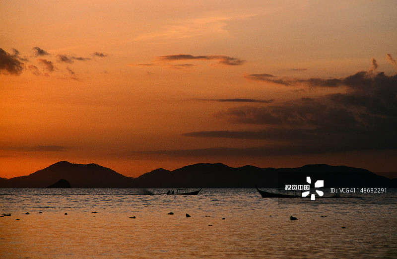 日落时海面上长尾船的剪影图片素材