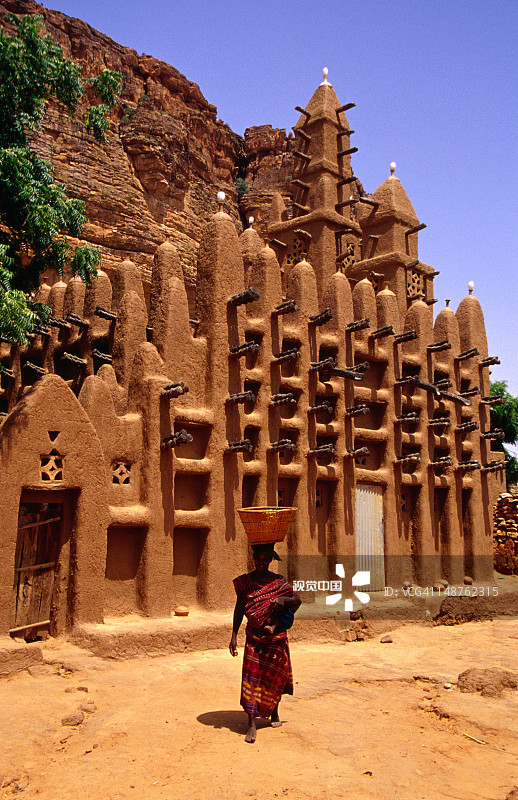 头顶篮子的女人走过萨赫勒风格的泥砖清真寺图片素材