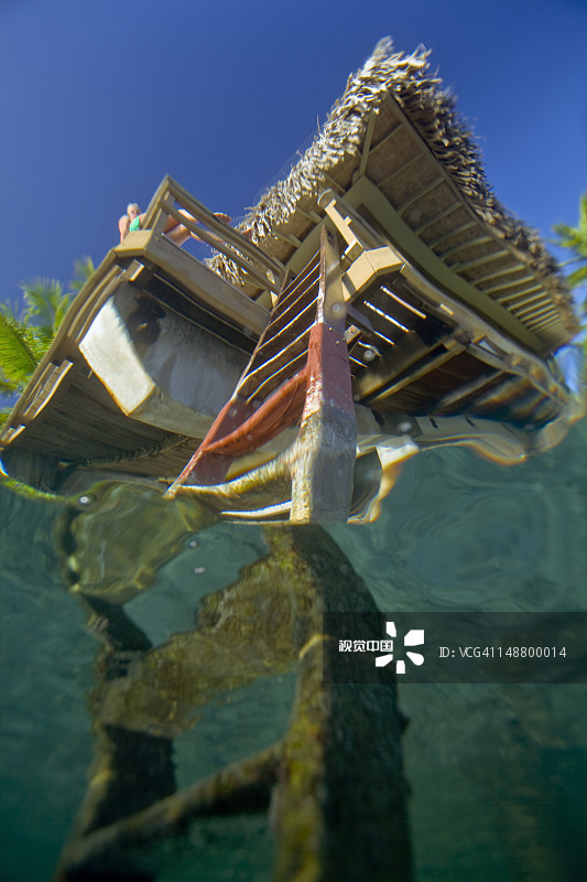 洲际水上小屋，从水面下方拍摄，一位年轻女士在阳台上享受日光浴。图片素材