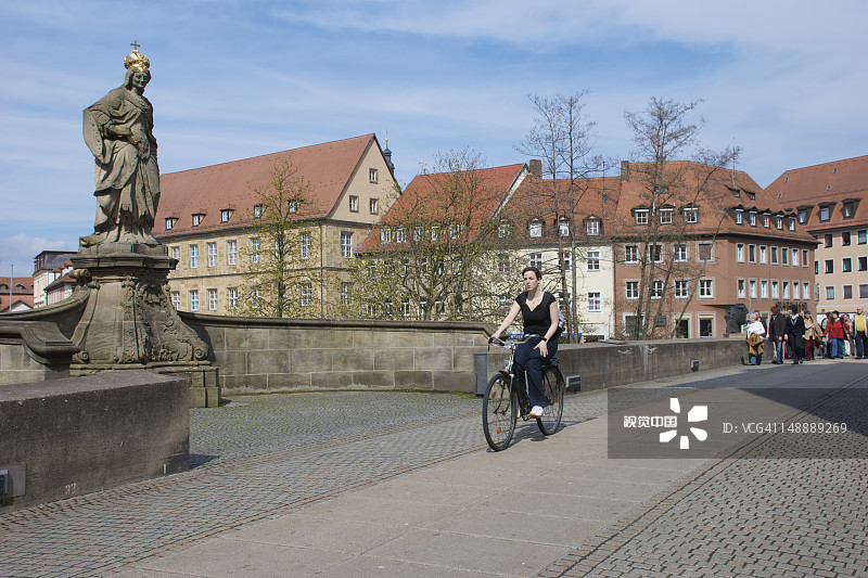 年轻女人骑自行车经过上桥的库尼根德雕像图片素材