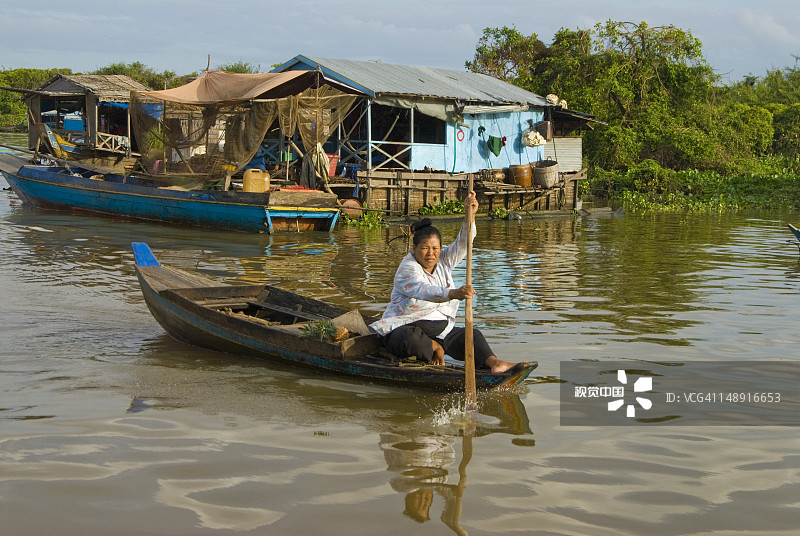 在洞里萨湖上划桨经过水上房屋的女人图片素材