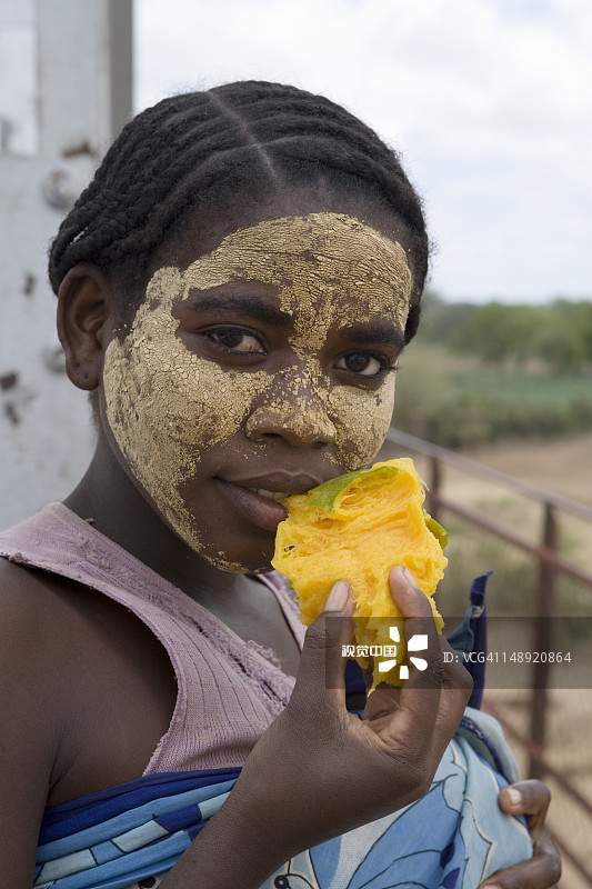 涂着黄色防晒油吃芒果的年轻女性肖像图片素材
