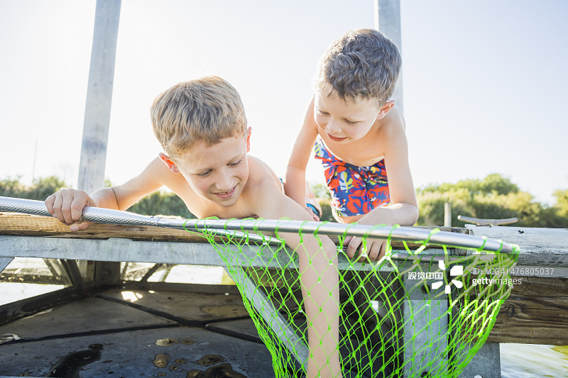 白人男孩在码头上用渔网捕鱼图片素材