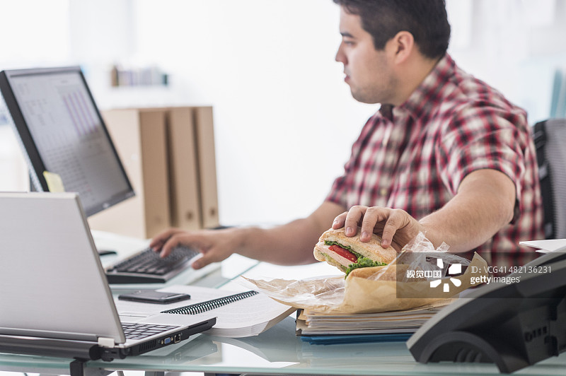 混血商人在办公桌前吃饭工作图片素材