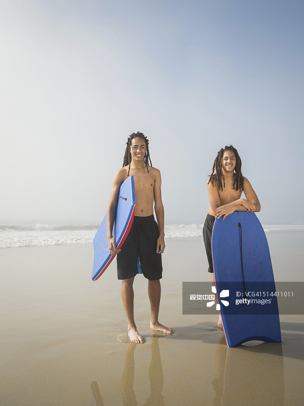 在海滩上带着冲浪板的黑人青少年男孩图片素材