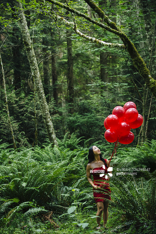 一个韩国女人在茂密的森林里拿着红气球图片素材