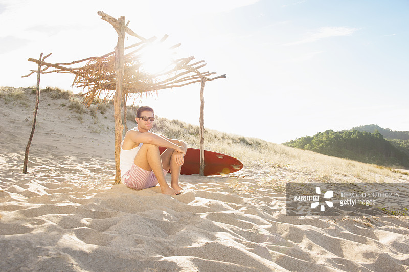 一名白人男子坐在沙滩上的木顶棚下图片素材