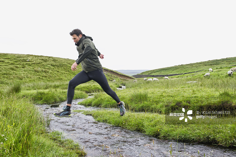 在乡村田野小溪上跳跃的白人男子图片素材