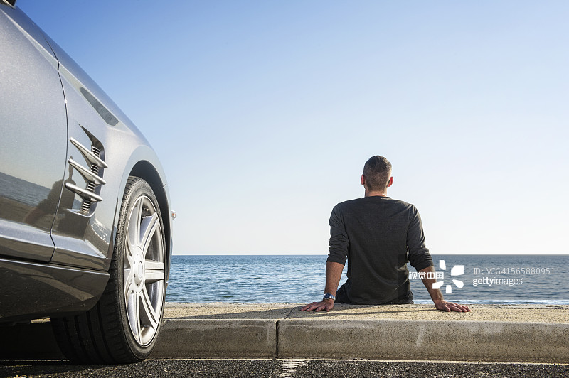西班牙裔男子在停车场欣赏汽车附近的海滩图片素材