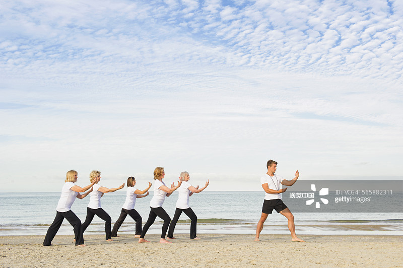 白人教练指导老年妇女在海滩上打太极图片素材
