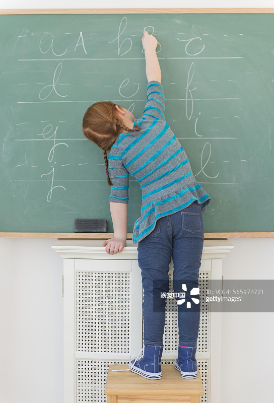 一个白人女孩在教室的黑板上写字图片素材