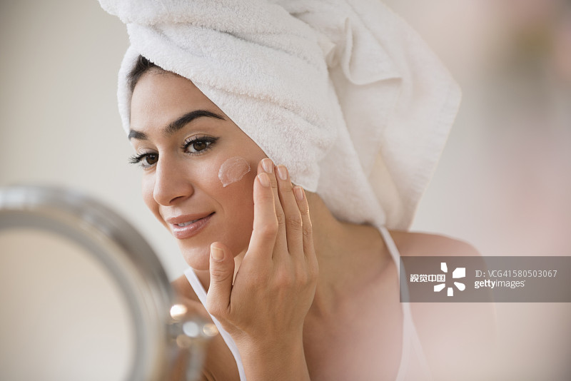 头发用毛巾裹着的女人在脸上擦乳液图片素材