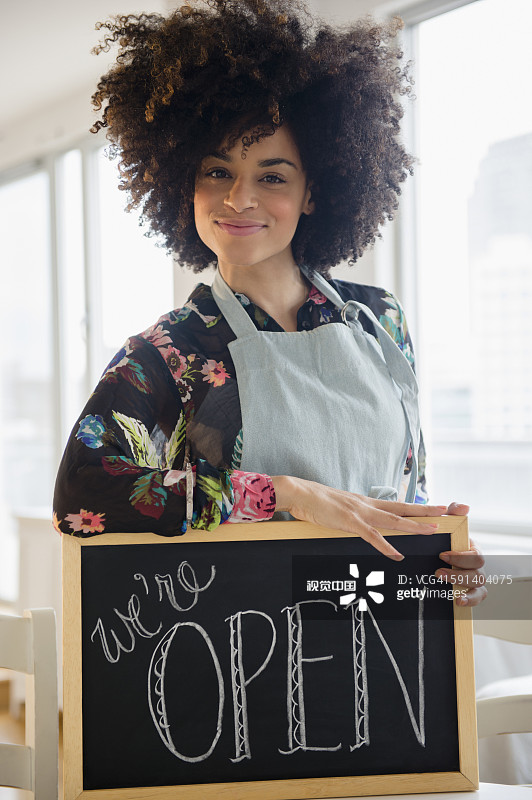 在咖啡馆里拿着“营业中”标志的混血女人图片素材