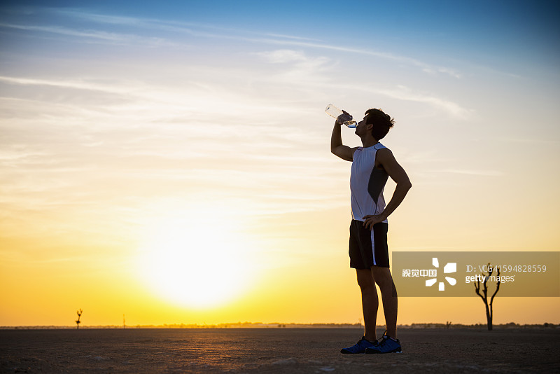 在沙漠中喝瓶装水的白人男人图片素材