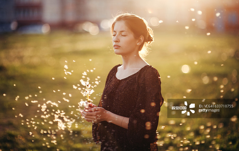 一个白人女人站在地里吹着蒲公英的种子图片素材