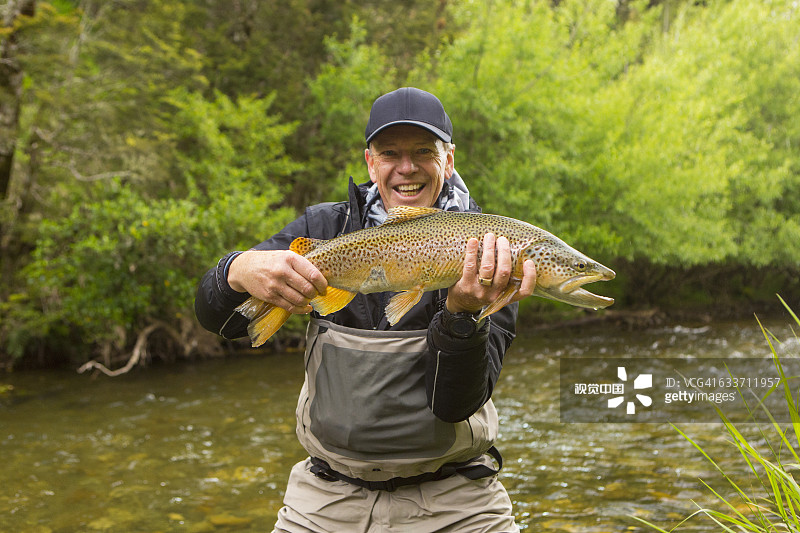 白人男子在偏远的河流中 holding fish图片素材
