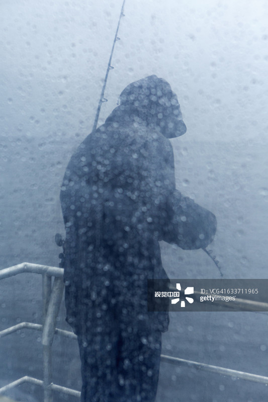 站在下着雨的船甲板上的白人渔夫图片素材