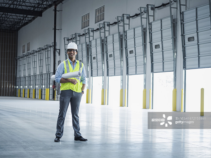 微笑的印度建筑师在开放式装货台门附近拿着蓝图图片素材