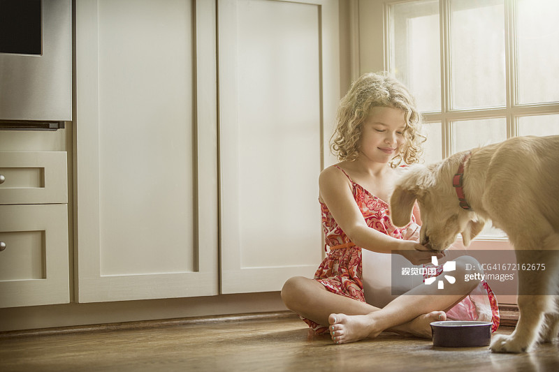 白人女孩坐在厨房地板上喂狗图片素材