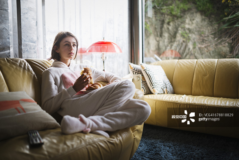 穿着兔子服装坐在沙发上吃羊角面包的混血女孩图片素材