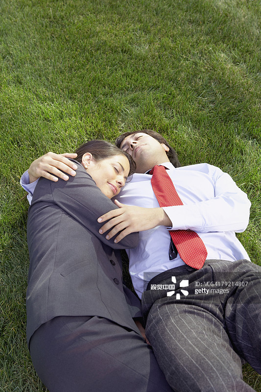 西班牙裔女商人和男商人躺在草地上拥抱，红木城，加利福尼亚州，美国图片素材