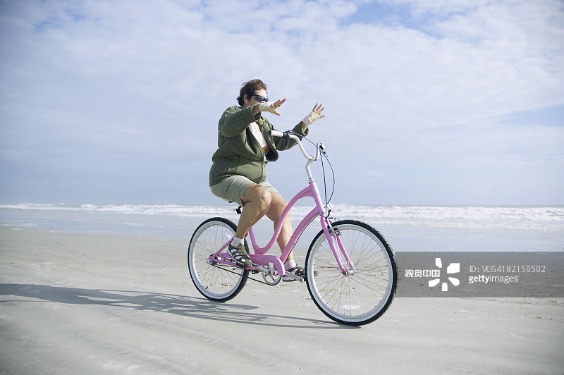 年长的女人在海滩上骑自行车图片素材