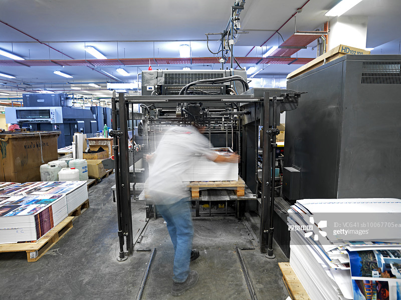 男工人在印刷厂操作印刷机（背面视角）图片素材