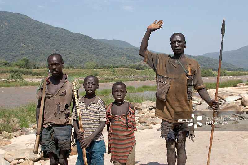 两个男孩（10-13岁）与手持矛、弓箭和步枪的男人站在青尼罗河边，肖像图片素材